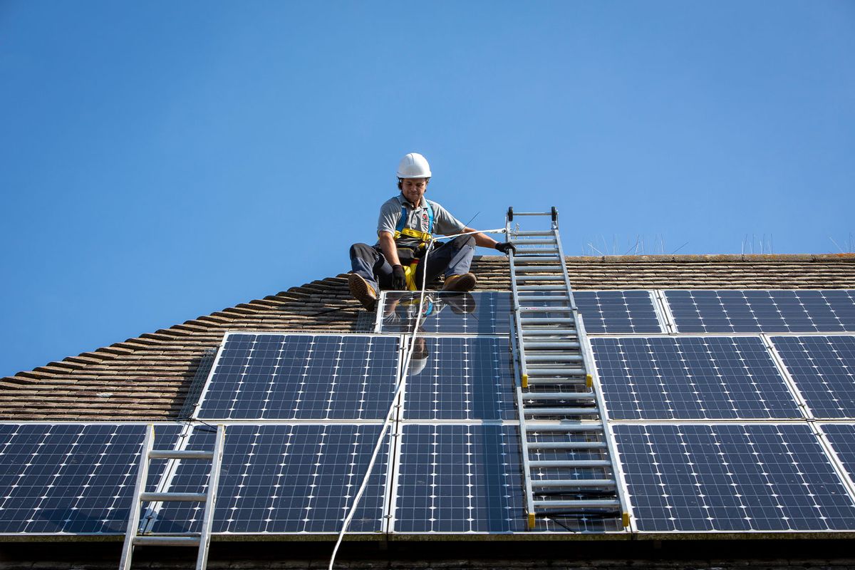 A maintenance person uses a ladder and harnesses to install equipment around a Solar panel array on the roof of a house. (Andrew Aitchison / In pictures via Getty Images)