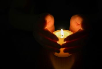 Hands protecting burning candle candlelight in darkness